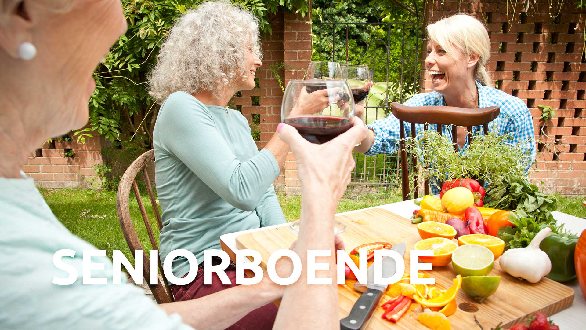 Tre kvinnor kring ett bord på en innergård. De ler och skålar i vin. På bordet finns frukt och grönsaker som de förbereder. 