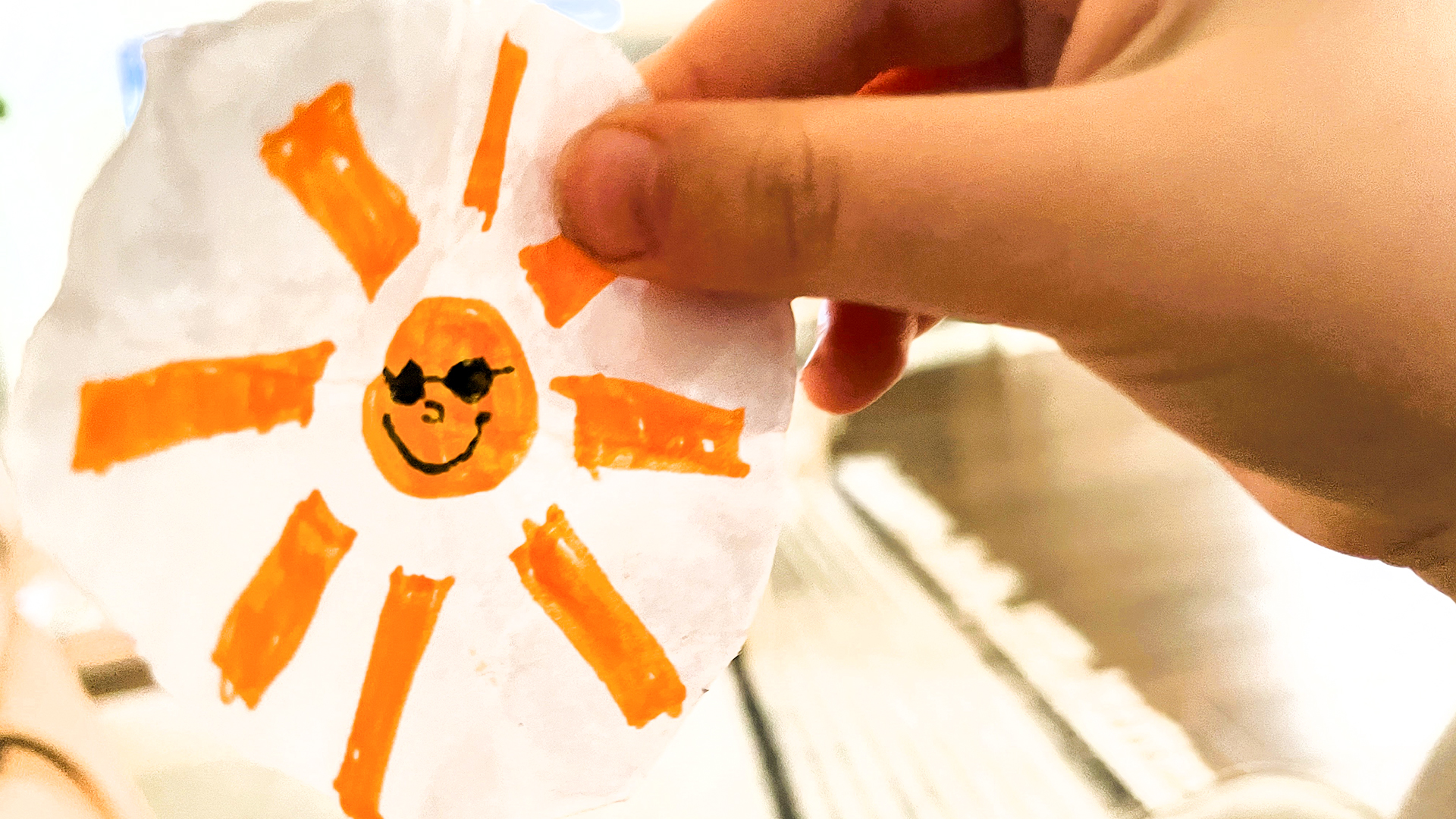 En hand som håller i en teckning med en sol på. 