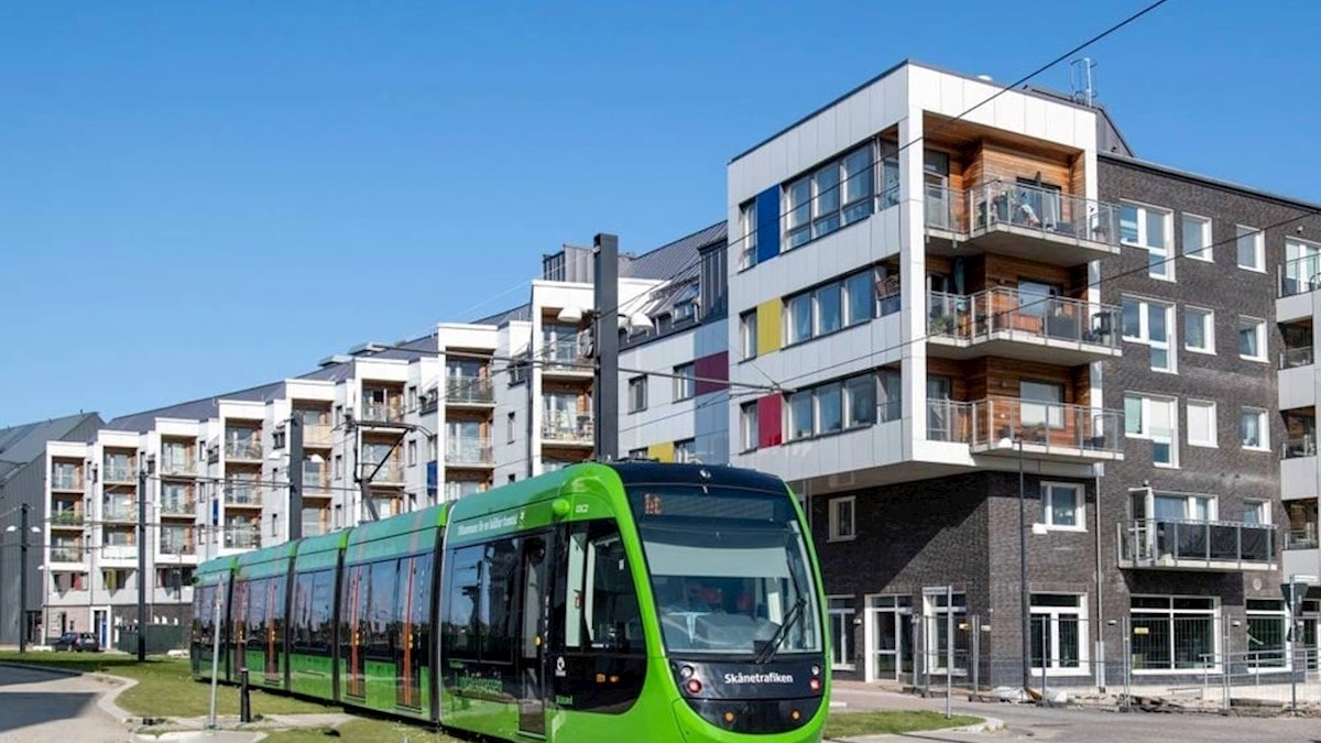 Grön spårvagn som passerar ett grått 5-våningshus