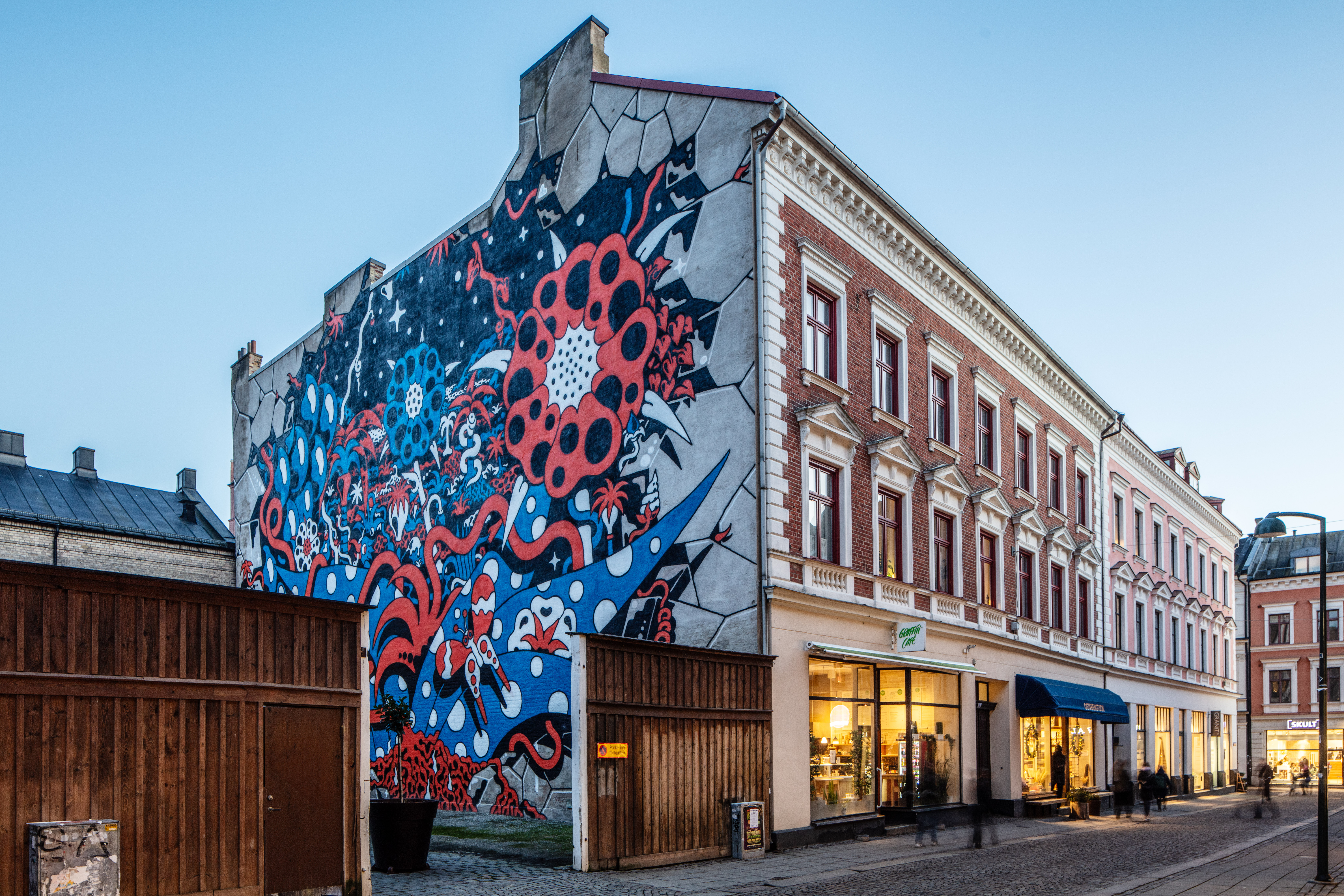 Mitt i bilden ser man brandgaveln på ett sekelskifteshus med muralmålningen i starka blå och röda färger 