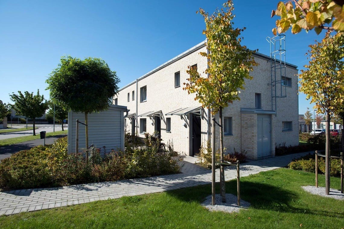 Radhus i två plan med ljus tegelfasad omringat av grönskande utemiljö