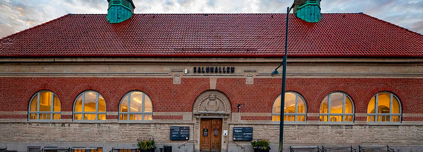 mitt framför entrén till Saluhallen. Solnedgång i bakgrunden. 