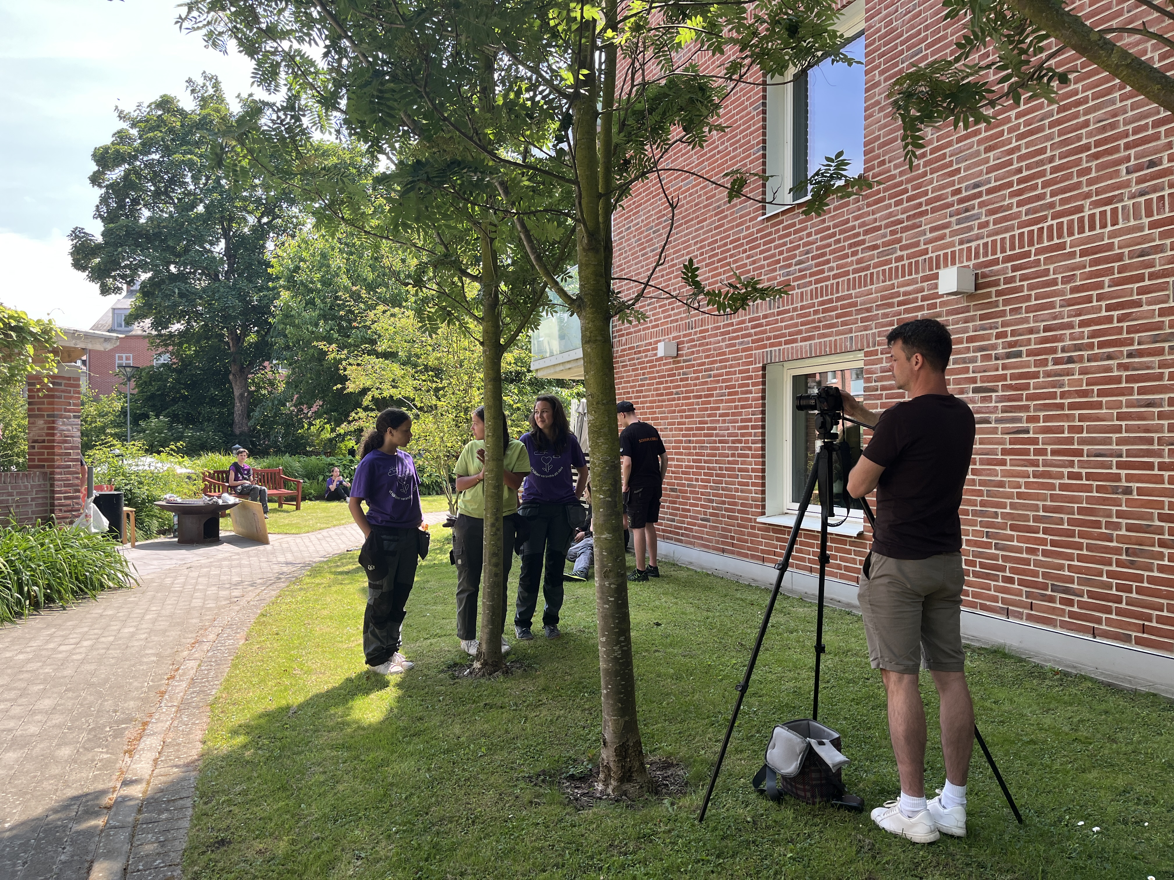fotograf justerar stativ i grön miljö med personer i bakgrunden