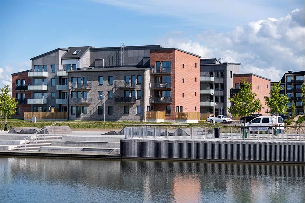 En modern bostadsbyggnad vid Råbysjön med tegel och mörka material, balkonger, parkerade bilar, och