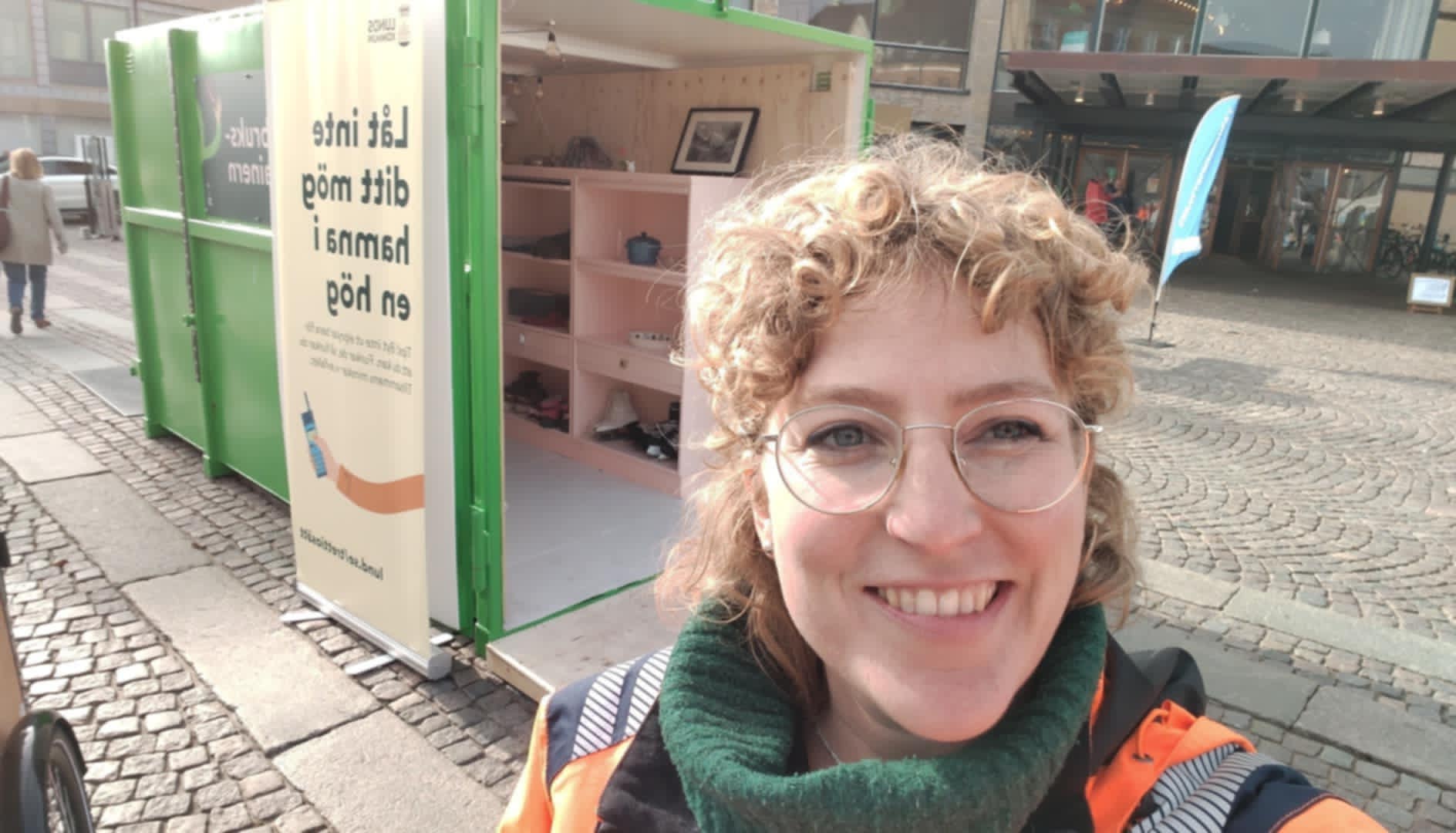 En kvinna på bild med en återbrukscontainer bakom sig.
