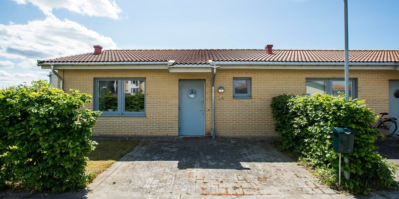 En del av en tegelbyggnad med balkonger, omgiven av grönska under en klar himmel. Byggnaden har fönster och dörrar som leder ut till de räckeomgivna balkongerna.