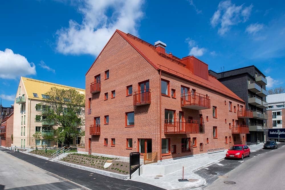 I förgrunden ett rött tegelhus med tre våningar, i bakgrunden ser man 6 våningshuset i svart sten