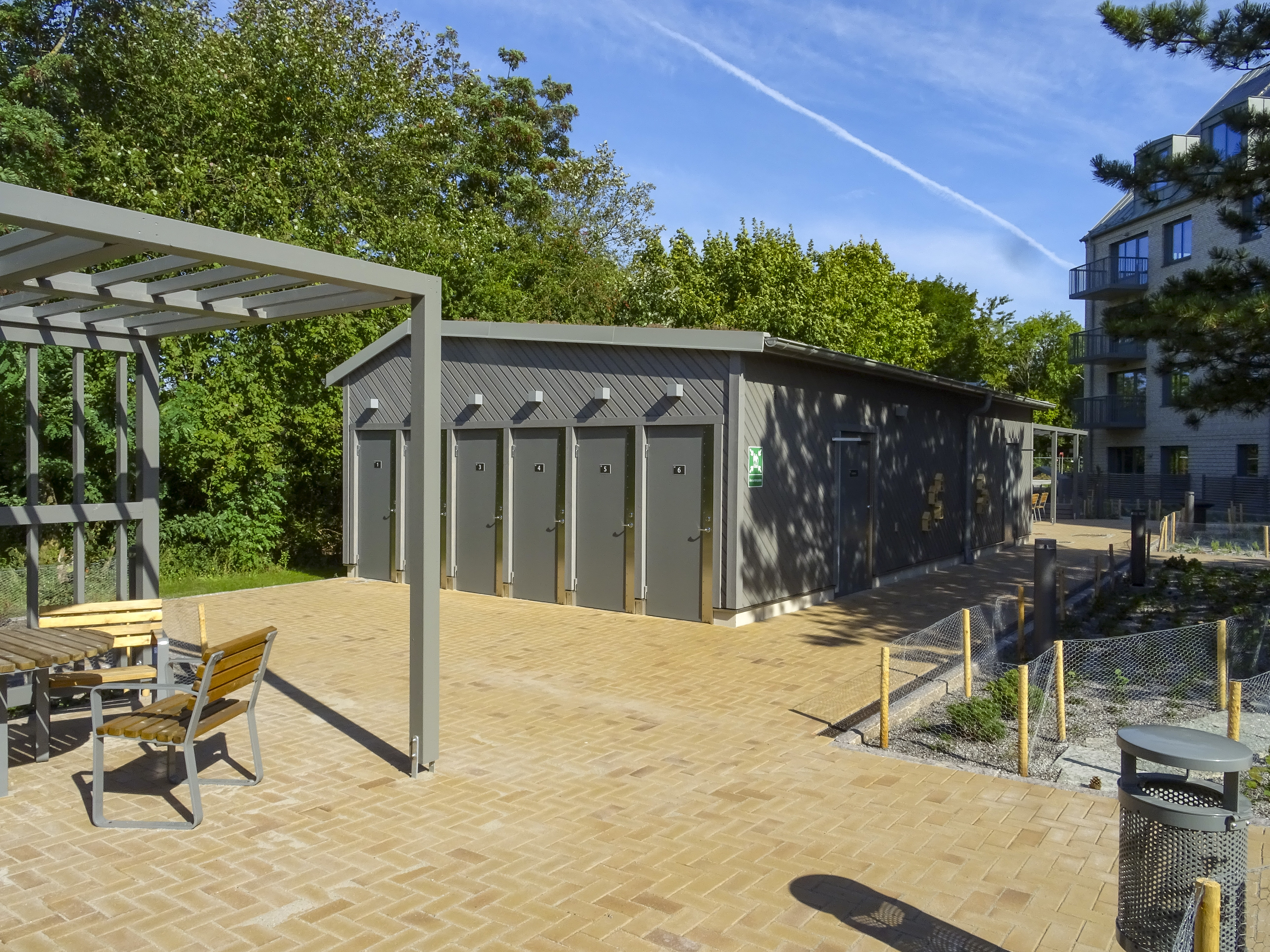 Innergården, till vänster skymtar en mindre sittplats med bord och stolar, mitt i bilden ser man cykelhuset med dörrarna till cykelboxarna.